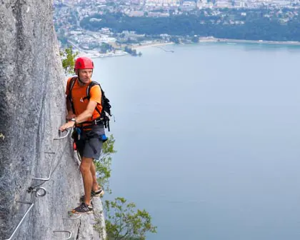 Nicolas regarde de lac du Bourget suspendu aux barreaux de la via ferrata du Col du Chat.